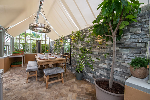 A Hartley Botanic Victorian Terrace Glasshouse incorporating an alfresco dining area, a wood burning stove and fragrant rambling rose. RHS Chelsea Flower Show, 2019