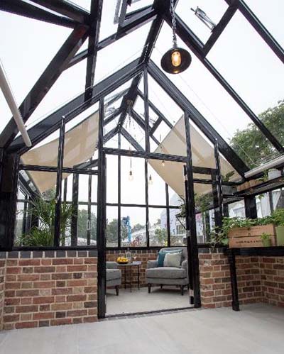 A Hartley Botanic Opus Grand Botanic Glasshouse at the 2021 RHS Chelsea Flower Show featuring a partitioned off relaxing area.