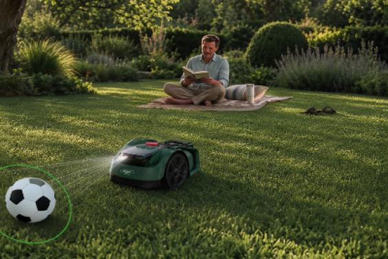 A robot lawn mower at work with a man sitting on the lawn nearby